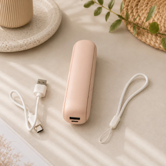 Compact pink portable fan folded for travel with USB charging cable and wrist strap on a neutral background.
