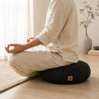 Angled view of black zafu meditation cushion with someone sitting down for better posture