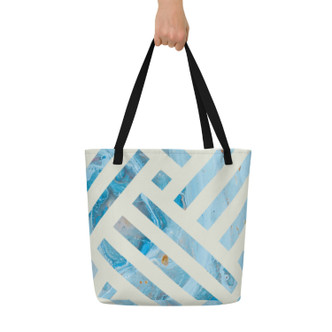Blue geometric tote bag with black straps held against a neutral background