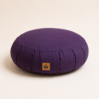 Purple Neuhaus Zen Comfort Zafu meditation cushion with organic cotton cover and buckwheat hull filling on a warm off-white studio background.