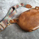 Close-up of brown faux leather waist bag showing textured finish, zip closure and colourful woven strap