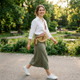 Woman wearing a brown leather and straw woven crossbody waist bag while walking outdoors in a park