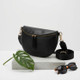 Black leather crossbody bag displayed in woven basket with fabric and design samples, showcasing craftsmanship