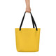 Yellow minimalist tote bag with black straps held against a neutral background