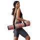 Woman carrying a rolled pink Deco yoga mat with a black shoulder strap