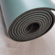 Rolled Signature teal green yoga mat showing its durable natural rubber construction and textured grip.