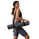 Woman carrying the rolled Geo Zen yoga mat with a black shoulder strap.