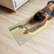 Woman stretching on a neutral retro stripe yoga mat with green, cream and yellow design
