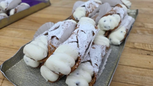 Large cannoli filled with ricotta cream and chocolate chips, dusted with powdered sugar