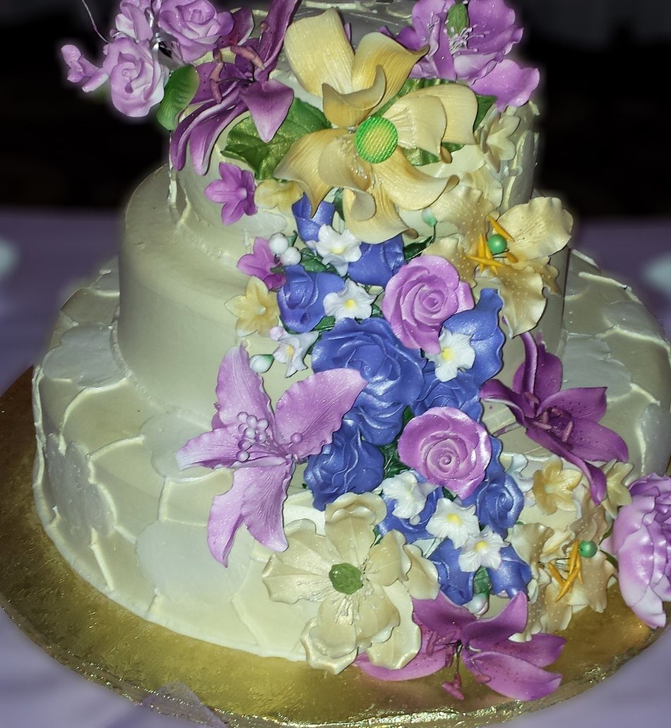 Two-tier cake covered in purple, blue and cream sugar flowers