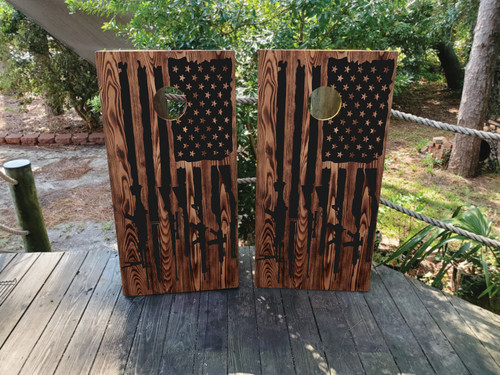 Cornhole wrap design with a wood grain background with a black USA flag and guns/rifles at the end of the flag