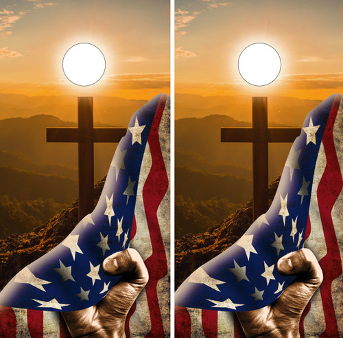 Pair of cornhole boards depicting a hand holding an American flag in front of a wooden cross on a hilltop at sunrise, with mountains in the background and a bright sun overhead, symbolizing faith and patriotism.