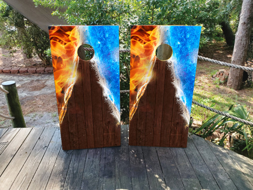 Pair of cornhole boards featuring a dynamic fire and ice split design at the top, transitioning into a dark woodgrain base with a vertical triangle spotlight effect.