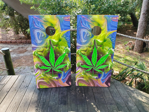 Pair of cornhole boards featuring a bold neon green cannabis leaf over a swirling psychedelic background of blues, greens, and purples, creating a vibrant and trippy visual.