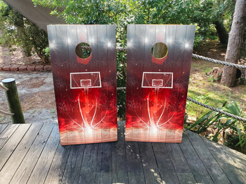Pair of cornhole boards featuring a stylized basketball hoop and backboard graphic with bright red and white light trails and particle effects, giving the impression of fast-paced action and energy.