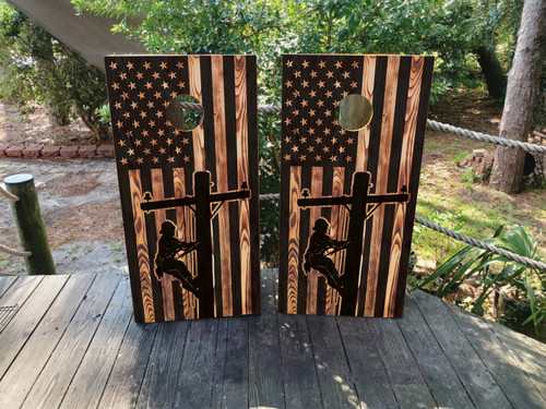 Cornhole boards featuring a wood grain USA flag with the silhouette of a lineman climbing up a pole