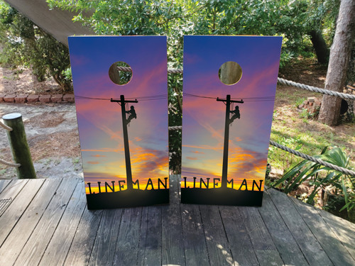 Cornhole boards featuring a silhouette of a lineman climbing a pole with a sunset background