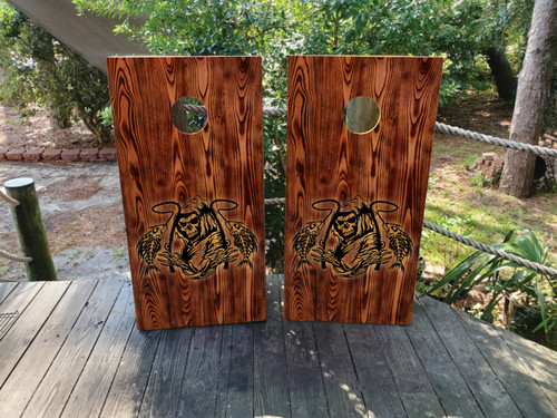Custom burned wood cornhole boards with fishing reaper design, outdoor setup