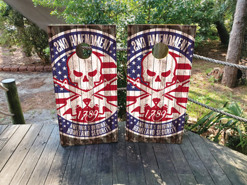 Cornhole boards on with a gray wood background and an american flag in the top corners. In the middle is a skull with 2nd amendment text