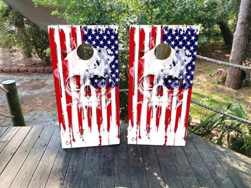 Pair of cornhole boards featuring a weathered American flag design with a white skull graphic overlay in the center, blending into the red stripes for a bold and gritty look.