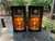 "Welcome to Our Firepit" cornhole boards with campfire design, marshmallows on sticks, and rustic wood background, placed outdoors on a wooden deck surrounded by greenery.