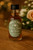 Wedding favor mini bottle with custom circular sage green label reading “Take a Shot, We’re Tying the Knot!” styled for a romantic rustic wedding table setting.