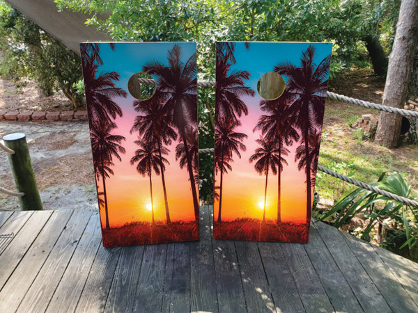 A colorful pink beach sunset scene with palm trees on a cornhole board