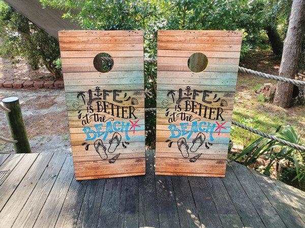 "Life is Better at the Beach Cornhole Boards featuring tropical beach scene with palm trees, ocean waves, and coastal typography"