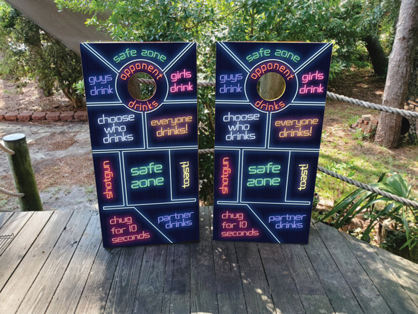 Cornhole boards featuring different phrases of a drinking game in neon colors. Phrases include safe zone, guys drink, girls drink, opponent drinks, choose who drinks, everyone drinks, shotgun, safe zone, toast, chug for 10 seconds, partner drinks