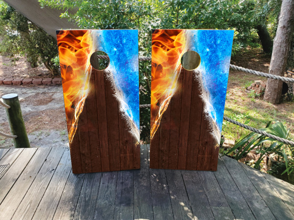 Pair of cornhole boards featuring a dynamic fire and ice split design at the top, transitioning into a dark woodgrain base with a vertical triangle spotlight effect.
