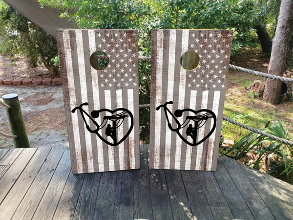 Two wooden boards with a rustic, faded American flag background featuring a black heart-shaped design that frames the silhouette of a lineman climbing a utility pole, symbolizing love, dedication, and pride in the profession.