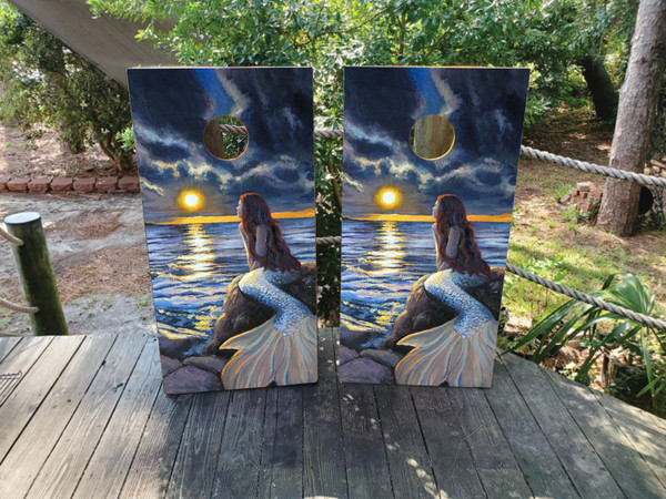 Cornhole boards featuring a mermaid sitting on a rock looking at a dark and cloudy sky