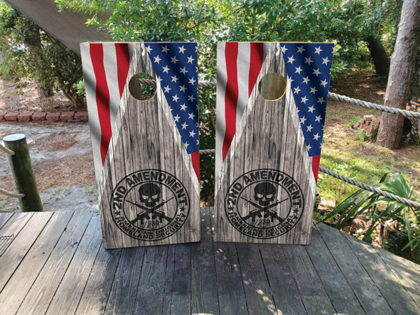 Cornhole boards on with a gray wood grain background and an american flag in the top corners. In the middle is a skull with 2nd amendment text