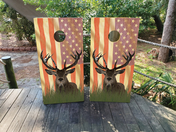 Two wooden boards featuring a rustic American flag background with faded stars and stripes, showcasing a large detailed buck with antlers in the foreground, standing in tall grass.