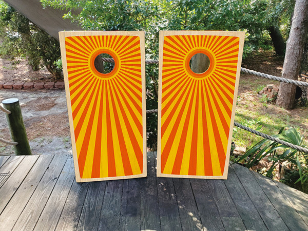 Cornhole boards featuring a sunburst orange and yellow pattern
