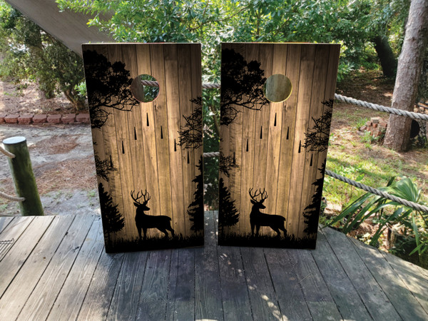 Two cornhole wraps with a rustic woodgrain background featuring black silhouettes of deer standing among trees, with bowling arrows descending from the top, creating a hunting and nature-inspired design."