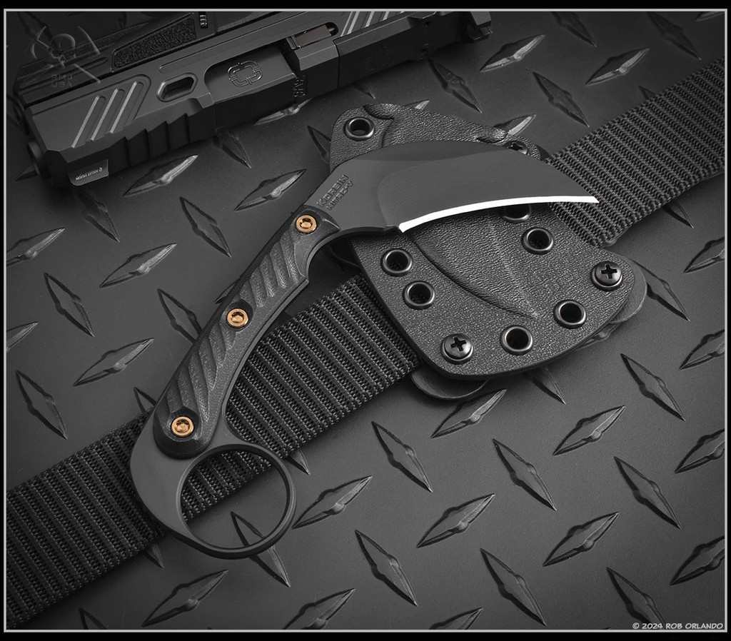 RMJ Tactical Korbin Karambit fixed blade knife - shown out of sheath reverse with sheath in background.  Graphite Black Cerakote Nitro-V stainless steel plain edge blade.  Black G-10 handle.  Model K-KO-BL-BL.
