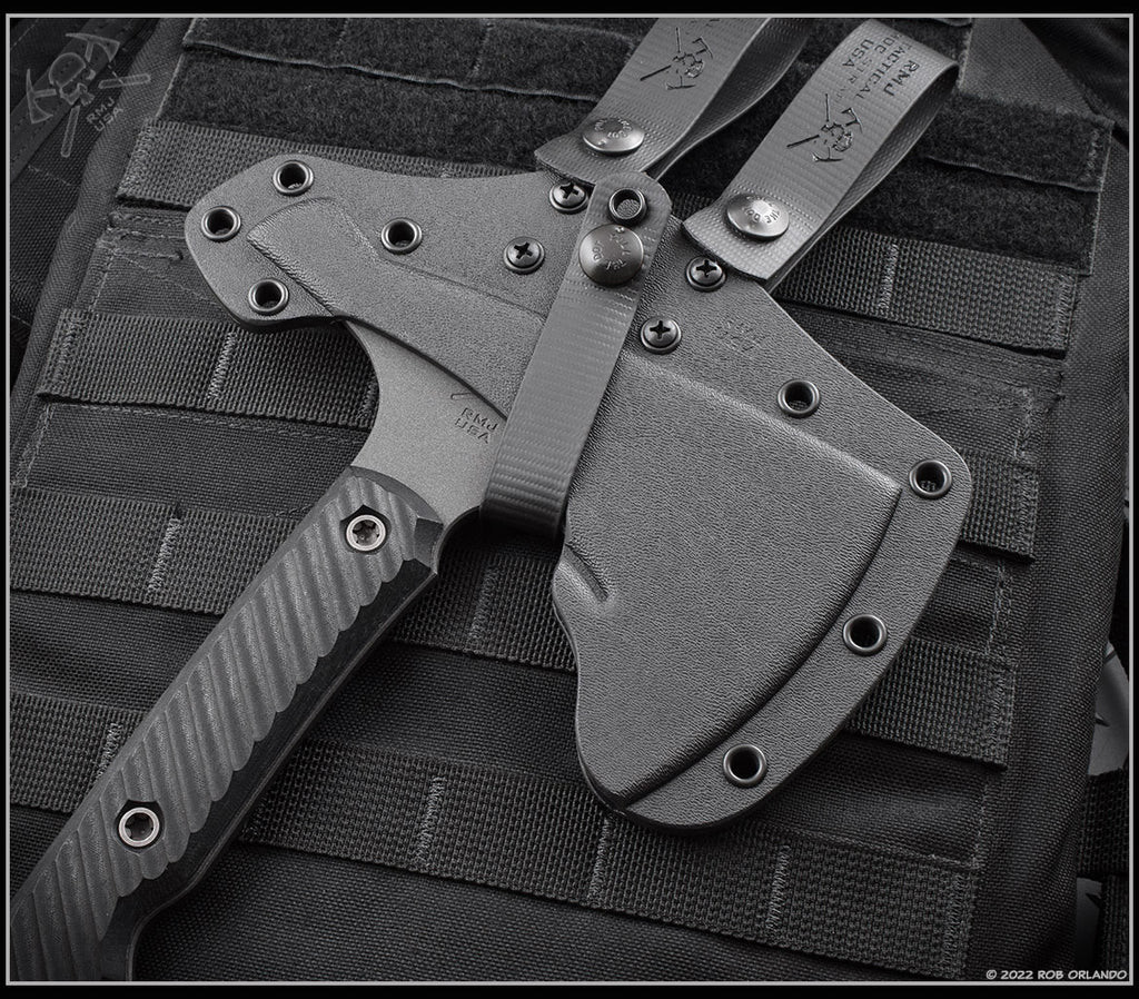 RMJ Tactical Tracker Dan Set - Gray Matter tomahawk shown in sheath obverse close up of head.   Cobalt Cerakote 80CRV2 steel plain head (tomahawk) and Cobalt Cerakote Nitro-V stainless steel plain edge blade (knife).  Black Linen Micarta handle.
For reference only.