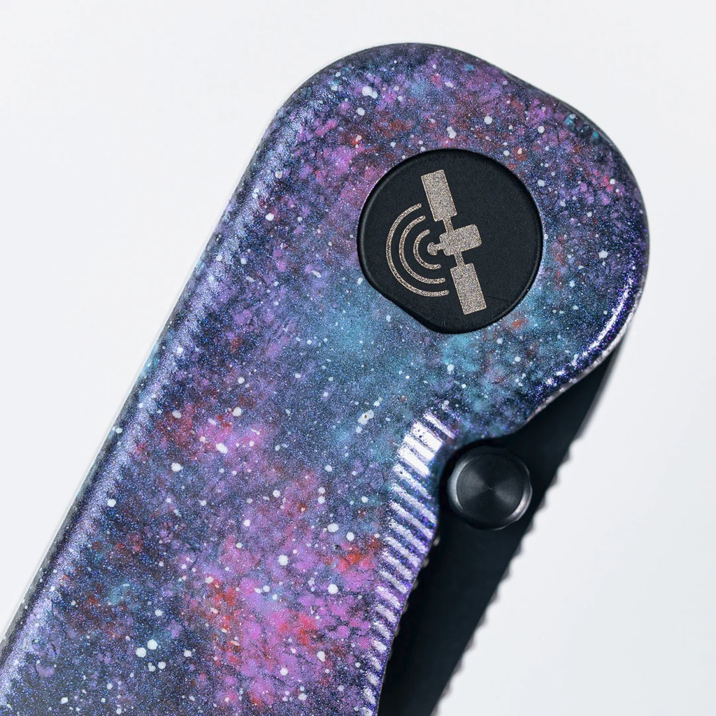 Tactile Knife Co Seasonal Release Deep Space Rockwall folding knife with thumb stud - shown close up of pivot.  Black MagnaCut stainless steel plain edge blade.  Deep Space themed titanium handle.
For reference only.