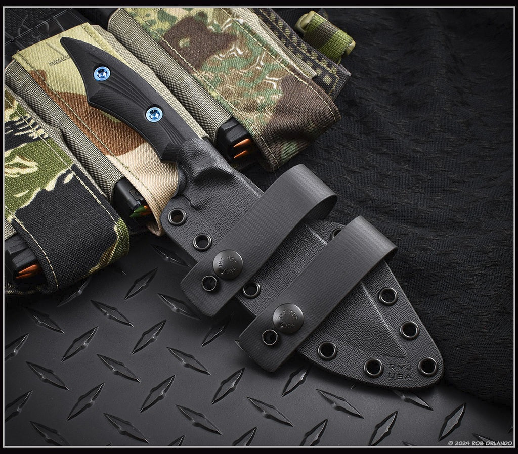 RMJ Tactical Ratatosk fixed blade knife with blue hardware installed - shown in sheath obverse.  Graphite Black Cerakote Nitro-V stainless steel plain edge blade.  Black Micarta handle.  Model K-RT-GB-LM-BK.
