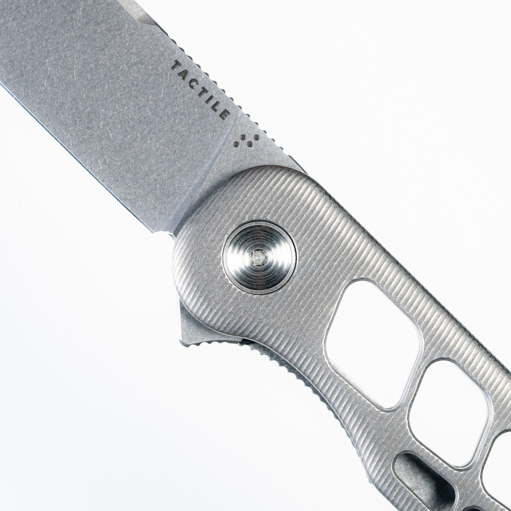 Tactile Knife Co Skeletonized Rockwall Flipper V2 folding knife with flipper tab - close up of presentation side pivot shown.  Stonewash MagnaCut stainless steel plain edge blade.  Stonewash titanium handle.  Model 20-GSW-MC01-TT01.