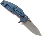 Rick Hinderer Knives Jurassic Slicer folding knife with thumb stud and flipper tab - shown open lock side.  Working Finish MagnaCut stainless steel plain edge blade.  Orange G-10 handle scale with Battle Blue lock side.  Model KJURSLMC.