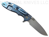Rick Hinderer Knives XM-18 Skinny Slicer with thumb stud and flipper tab - shown open lock side.  Stonewash Magnacut stainless steel, hollow ground, plain edge blade.  Black G-10 handle with stonewash blue lock side. 