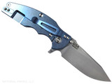 Rick Hinderer Knives Jurassic Hollow Grind Slicer folding knife with flipper tab - shown open lock side.  Stonewash MagnaCut stainless steel plain edge blade.  Black G-10 handle scale with stonewash blue titanium lock side.  Model KJURSLHO.