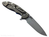 Rick Hinderer Knives XM-18 3.5" Spanto folding knife with thumb stud and flipper tab - shown open lock side.  Working Finish 20CV stainless steel plain edge blade.  Blue - black G-10 handle with Battle Bronze lock side.  Model KXM35SPA.