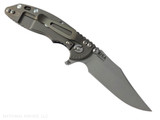 Rick Hinderer Knives XM-18 3.0" Bowie folding knife with thumb stud and flipper tab - shown open lock side.  Working Finish 20CV stainless steel plain edge blade.  Black G-10 handle with Battle Bronze lock side.  Model KXM30BOW.
