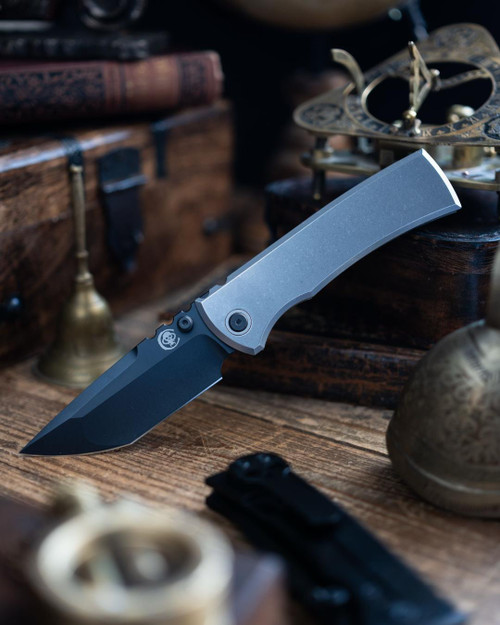 Chaves Knives Integral Redencion 229 folding knife featuring a thumb stud - shown open presentation side.  Black PVD coated M390 stainless steel Tanto style plain edge blade.  Bright titanium handle.  Model CK-1C1-2G1A-11AOI