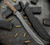 RMJ Tactical Wyvern fixed blade short sword - shown out of sheath obverse with sheath next to Wyvern.  Tungsten Cerakote 3V steel plain edge blade.  Hyena Brown G-10 handle. 