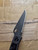 Used Spyderco Police folding knife with thumb hole - shown close up of pocket clip side blade.  Black VG-10 stainless steel plain edge blade.  Black stainless steel handle.  Model C07BKP.