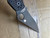 Used Spyderco Military 2 Salt folding knife with thumb hole - close up of pocket clip side blade shown.  Black CPM MagnaCut stainless steel plain edge blade.  Black G-10 handle.  Model C36GMCBKP2.